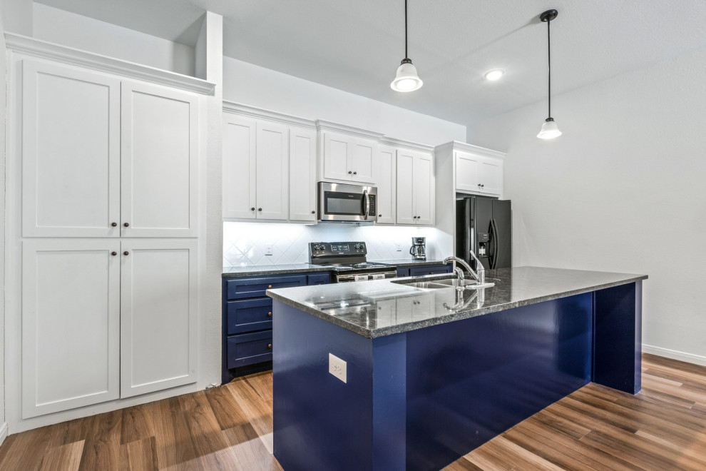 Modern inredning av ett mellanstort svart svart kök, med en undermonterad diskho, skåp i shakerstil, blå skåp, granitbänkskiva, vitt stänkskydd, stänkskydd i keramik, rostfria vitvaror, ljust trägolv, en köksö och brunt golv