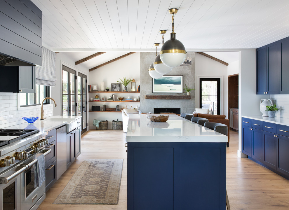 Design ideas for a medium sized traditional u-shaped open plan kitchen in Austin with shaker cabinets, blue cabinets, engineered stone countertops, white splashback, ceramic splashback, stainless steel appliances, medium hardwood flooring, an island, white worktops, a belfast sink and brown floors.