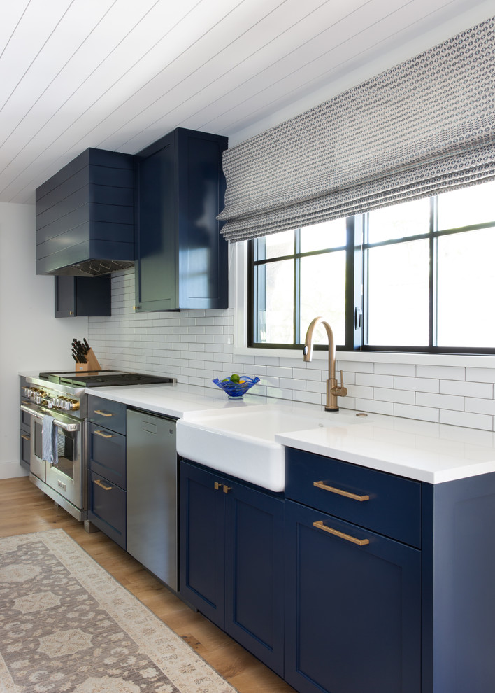 Mid-sized trendy u-shaped medium tone wood floor open concept kitchen photo in Austin with an undermount sink, shaker cabinets, blue cabinets, quartz countertops, white backsplash, ceramic backsplash, stainless steel appliances, an island and white countertops