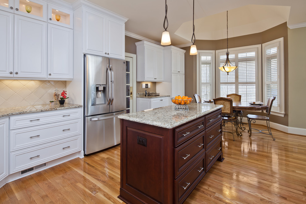 Mid-sized elegant u-shaped light wood floor eat-in kitchen photo in Charlotte with an undermount sink, raised-panel cabinets, white cabinets, granite countertops, beige backsplash, ceramic backsplash, stainless steel appliances and an island