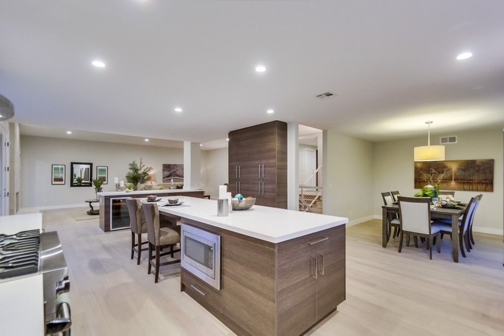 Inspiration for a large contemporary u-shaped kitchen/diner in San Diego with flat-panel cabinets, grey cabinets, quartz worktops, white splashback, glass tiled splashback, stainless steel appliances, light hardwood flooring and an island.