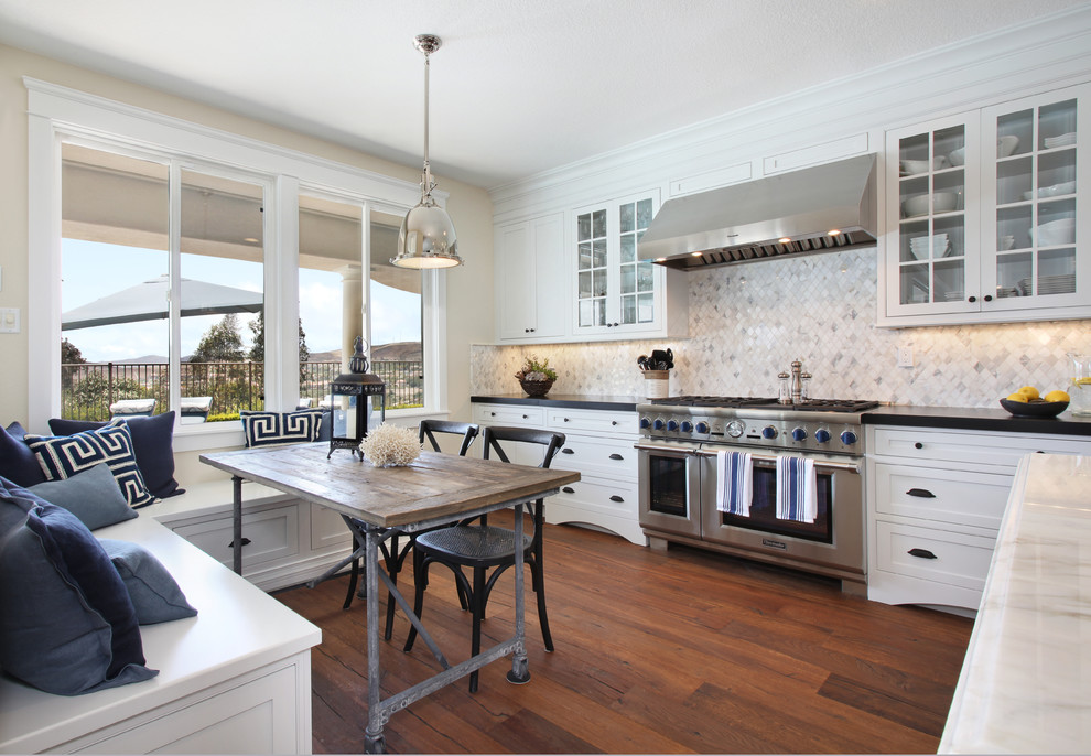 Eat-in kitchen - large transitional l-shaped medium tone wood floor eat-in kitchen idea in Orange County with a farmhouse sink, beaded inset cabinets, white cabinets, marble countertops, white backsplash, mosaic tile backsplash, stainless steel appliances and an island