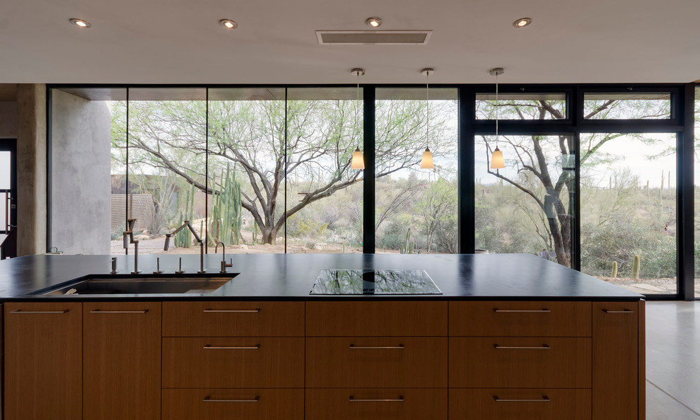 Idée de décoration pour une grande cuisine parallèle minimaliste en bois clair avec un évier encastré, un placard à porte plane, un électroménager en acier inoxydable et sol en béton ciré.