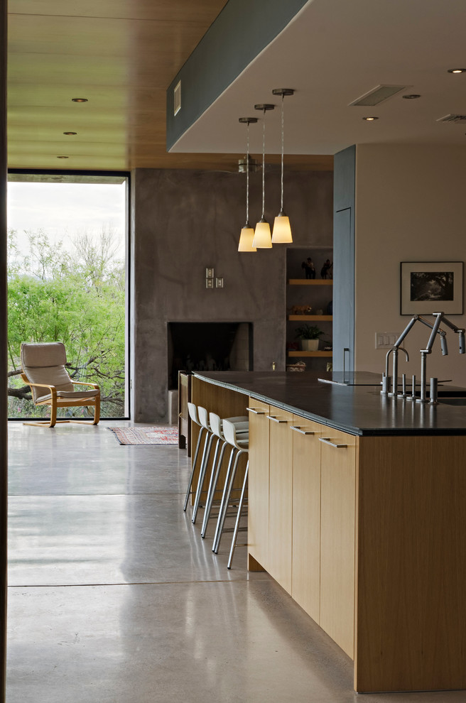 Modelo de cocina minimalista grande con fregadero bajoencimera, armarios con paneles lisos, puertas de armario de madera clara, electrodomésticos de acero inoxidable y suelo de cemento
