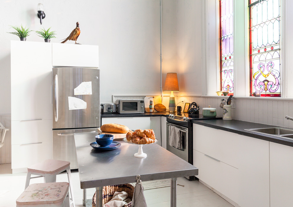 Bild på ett funkis kök, med en nedsänkt diskho, släta luckor, vita skåp, fönster som stänkskydd, rostfria vitvaror, målat trägolv, en köksö och vitt golv