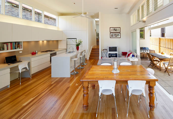 Medium sized contemporary galley open plan kitchen in Sydney with a double-bowl sink, flat-panel cabinets, white cabinets, engineered stone countertops, beige splashback, glass sheet splashback, medium hardwood flooring and an island.