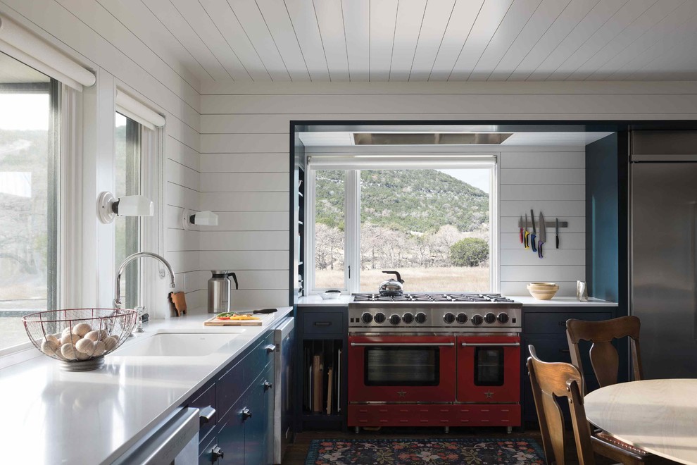 Design ideas for a rural l-shaped kitchen/diner in Austin with a submerged sink, flat-panel cabinets, blue cabinets, engineered stone countertops, white splashback, wood splashback, coloured appliances, dark hardwood flooring, no island, brown floors and white worktops.