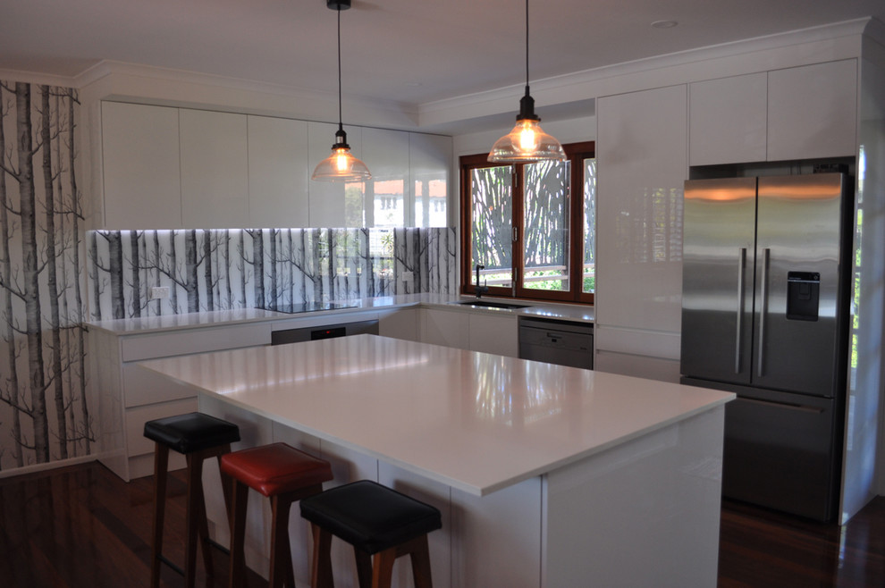 Modern inredning av ett mellanstort kök, med en undermonterad diskho, släta luckor, vita skåp, bänkskiva i kvarts, flerfärgad stänkskydd, glaspanel som stänkskydd, rostfria vitvaror, mörkt trägolv och en köksö