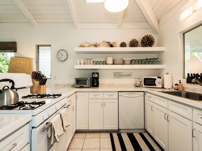 Geschlossene Küche in U-Form mit Waschbecken, Schrankfronten im Shaker-Stil, weißen Schränken, Küchenrückwand in Weiß, Rückwand aus Stein und weißen Elektrogeräten in Hawaii