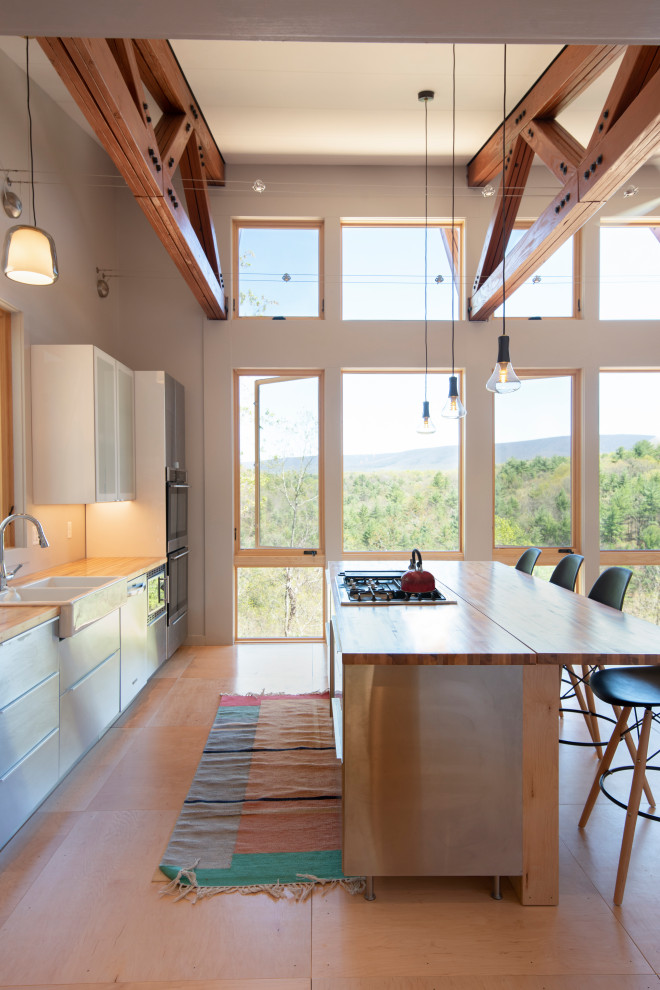 Modern inredning av ett kök och matrum, med en rustik diskho, skåp i rostfritt stål, träbänkskiva, rostfria vitvaror, plywoodgolv och en köksö