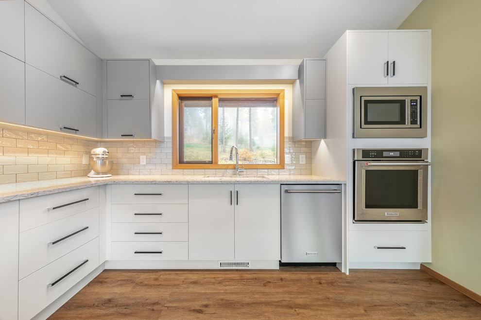 Foto på ett mellanstort funkis kök, med en undermonterad diskho, släta luckor, grå skåp, granitbänkskiva, vitt stänkskydd, stänkskydd i tunnelbanekakel, rostfria vitvaror och en köksö