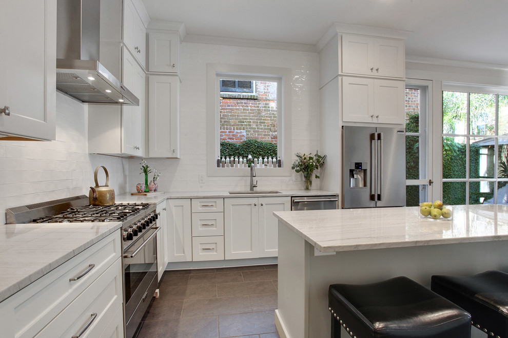 Kitchen - large transitional l-shaped ceramic tile and brown floor kitchen idea in New Orleans with an undermount sink, shaker cabinets, white cabinets, quartzite countertops, white backsplash, subway tile backsplash, stainless steel appliances, an island and white countertops