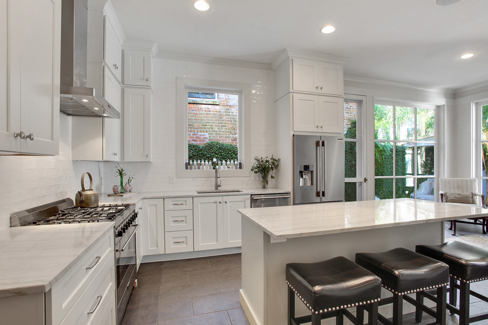 Kitchen - large transitional l-shaped ceramic tile and brown floor kitchen idea in New Orleans with an undermount sink, shaker cabinets, white cabinets, quartzite countertops, white backsplash, subway tile backsplash, stainless steel appliances, an island and white countertops