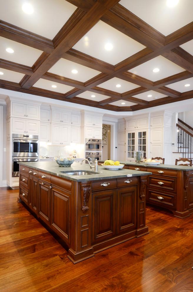 Huge elegant u-shaped medium tone wood floor and brown floor enclosed kitchen photo in Other with an undermount sink, raised-panel cabinets, white cabinets, white backsplash, porcelain backsplash, stainless steel appliances, two islands, marble countertops and white countertops