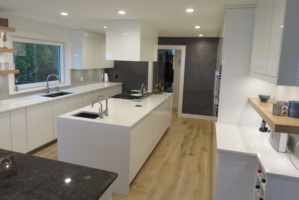 Contemporary u-shaped kitchen in Vancouver with a submerged sink, flat-panel cabinets, white cabinets, quartz worktops, white splashback, light hardwood flooring and multiple islands.