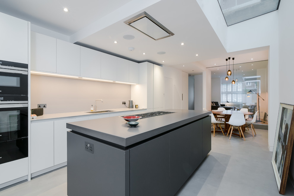 Diseño de cocina comedor contemporánea de tamaño medio con fregadero bajoencimera, armarios con paneles lisos, puertas de armario negras, encimera de acrílico, salpicadero beige, salpicadero de vidrio templado, electrodomésticos de acero inoxidable, suelo de cemento, una isla y suelo gris