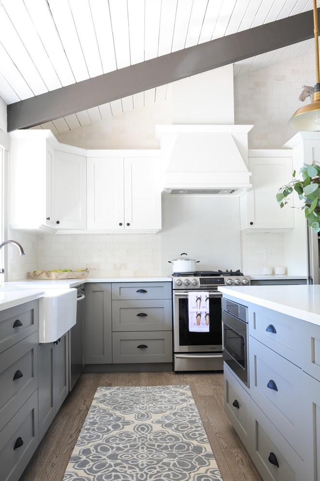 Example of a cottage l-shaped light wood floor and brown floor open concept kitchen design in Other with a farmhouse sink, shaker cabinets, gray cabinets, solid surface countertops, brick backsplash, stainless steel appliances, an island and white backsplash