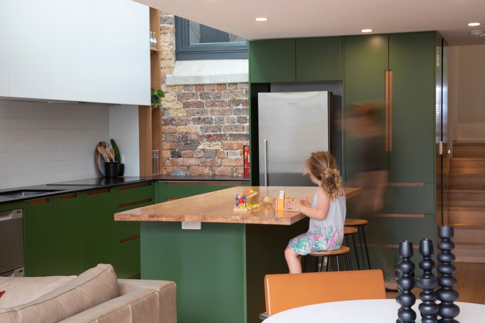 Offene Moderne Küche in L-Form mit Unterbauwaschbecken, flächenbündigen Schrankfronten, grünen Schränken, Küchenrückwand in Weiß, Küchengeräten aus Edelstahl, braunem Holzboden, Kücheninsel, braunem Boden und schwarzer Arbeitsplatte in Sydney