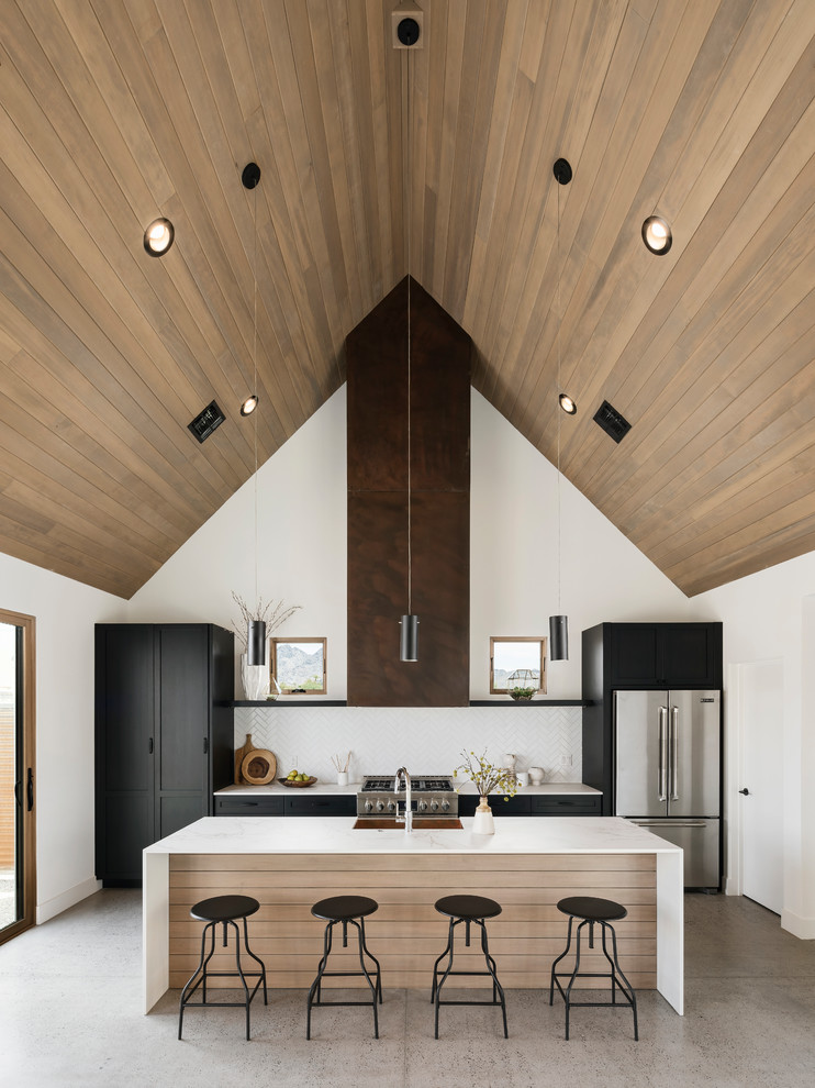 Exempel på ett amerikanskt linjärt kök med öppen planlösning, med en rustik diskho, luckor med infälld panel, svarta skåp, bänkskiva i kvarts, vitt stänkskydd, stänkskydd i keramik, rostfria vitvaror, betonggolv, en köksö och grått golv