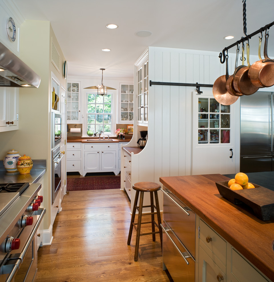 Klassische Küche mit Unterbauwaschbecken, Glasfronten, weißen Schränken, Küchengeräten aus Edelstahl, braunem Holzboden, Kücheninsel und Arbeitsplatte aus Holz in Philadelphia