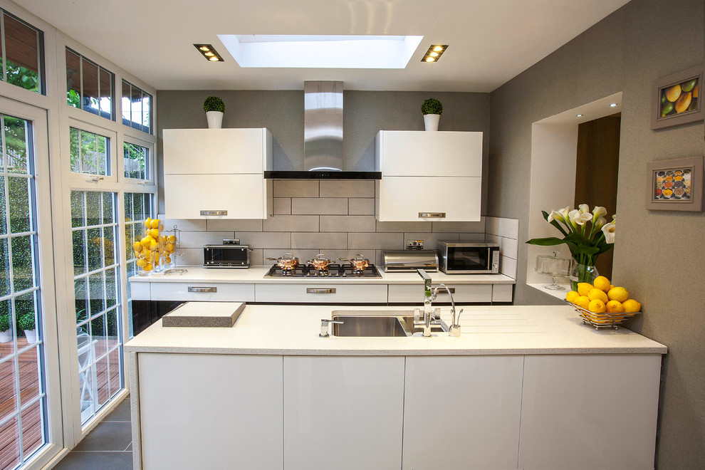 Photo of a small contemporary galley kitchen in London with a double-bowl sink, flat-panel cabinets, white cabinets, white splashback, metro tiled splashback and a breakfast bar.