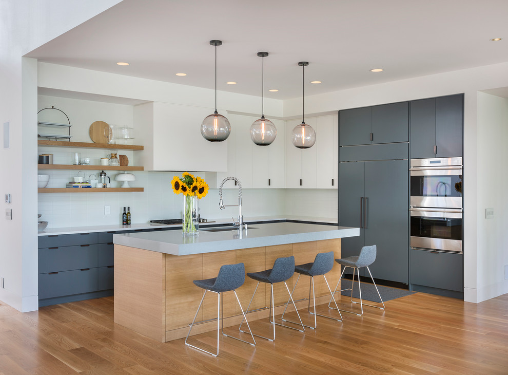 Moderne Küche in L-Form mit Unterbauwaschbecken, flächenbündigen Schrankfronten, grauen Schränken, Küchenrückwand in Weiß, Elektrogeräten mit Frontblende, hellem Holzboden und Kücheninsel in Portland
