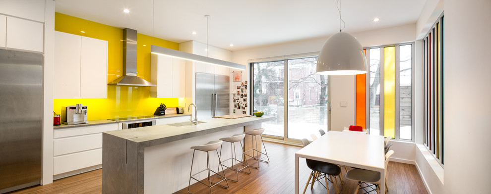 Zweizeilige Moderne Wohnküche mit Unterbauwaschbecken, flächenbündigen Schrankfronten, weißen Schränken, Küchenrückwand in Gelb, Glasrückwand und Küchengeräten aus Edelstahl in Ottawa