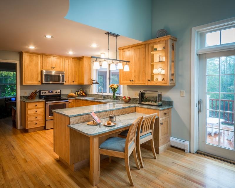 Kleine Küche in U-Form mit Unterbauwaschbecken, hellen Holzschränken, Granit-Arbeitsplatte, Küchengeräten aus Edelstahl und hellem Holzboden in New York