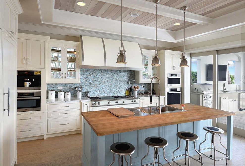 Inspiration for a large l-shaped kitchen/diner in New York with white cabinets, wood worktops, blue splashback, stainless steel appliances, light hardwood flooring and an island.