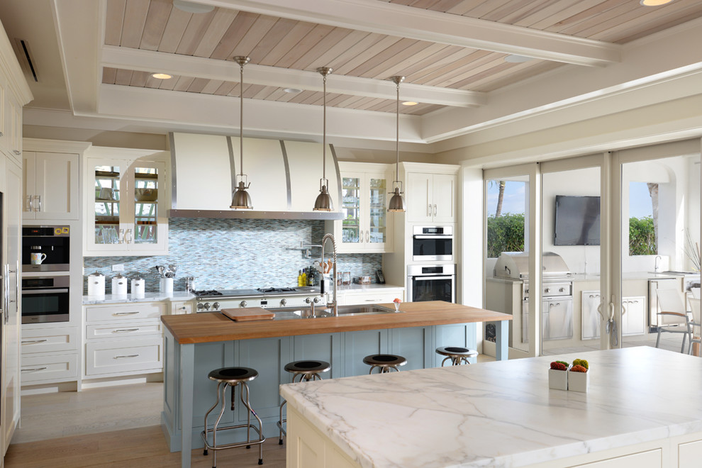 Photo of an expansive coastal l-shaped kitchen/diner in Miami with flat-panel cabinets, white cabinets, blue splashback, stainless steel appliances, light hardwood flooring and multiple islands.