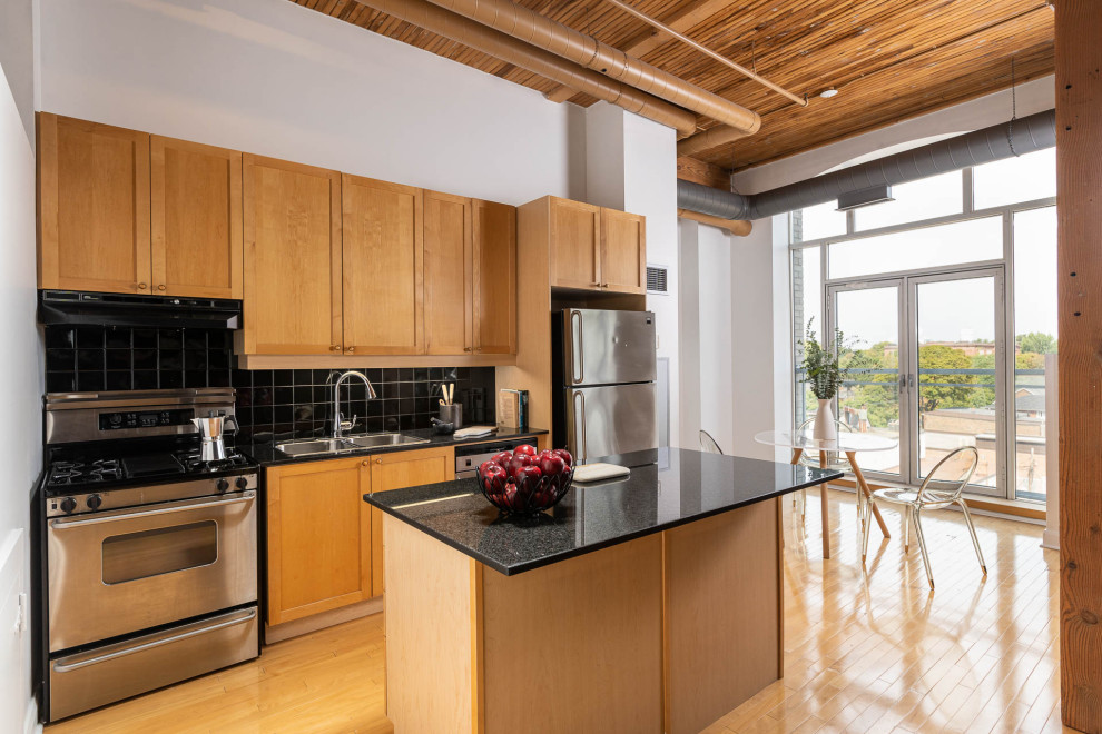 Transitional medium tone wood floor and brown floor eat-in kitchen photo in Toronto with a double-bowl sink, shaker cabinets, medium tone wood cabinets, black backsplash, stainless steel appliances, an island and black countertops