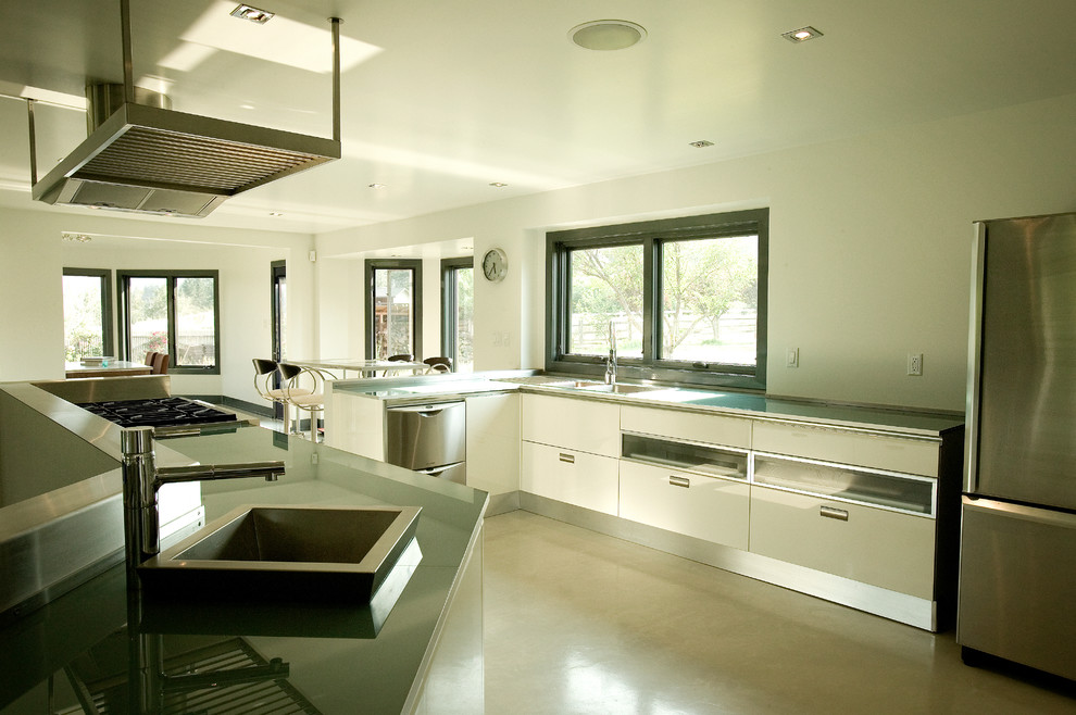 Idéer för att renovera ett stort funkis kök, med en nedsänkt diskho, släta luckor, skåp i rostfritt stål, bänkskiva i rostfritt stål, rostfria vitvaror, betonggolv, en halv köksö och grått golv