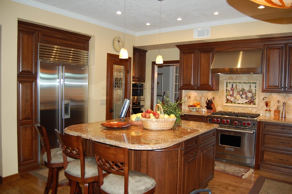 Example of a classic kitchen design in Los Angeles with stainless steel appliances, raised-panel cabinets, dark wood cabinets, granite countertops, beige backsplash and stone tile backsplash