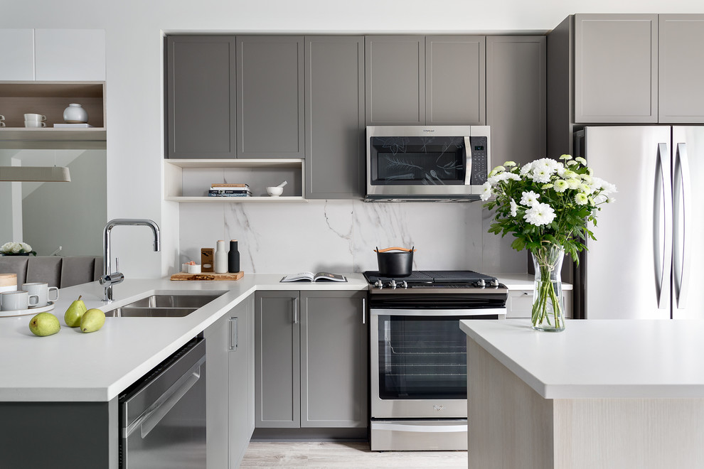 This is an example of a scandinavian l-shaped kitchen/diner in Vancouver with a submerged sink, shaker cabinets, grey cabinets, engineered stone countertops, white splashback, porcelain splashback, stainless steel appliances, laminate floors, an island, grey floors and white worktops.