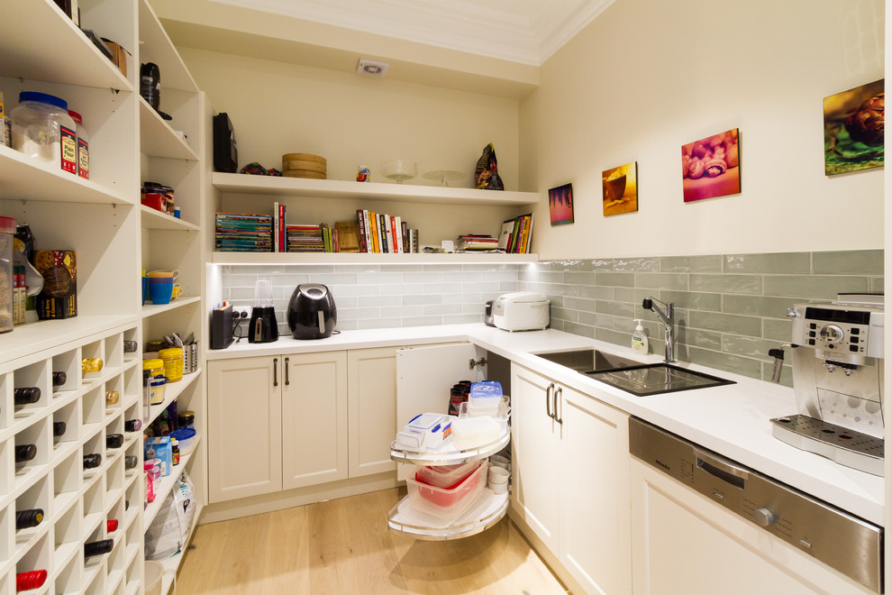 Klassisk inredning av ett mellanstort vit vitt kök, med en undermonterad diskho, skåp i shakerstil, vita skåp, bänkskiva i kvarts, grönt stänkskydd, stänkskydd i tunnelbanekakel, svarta vitvaror, ljust trägolv, en köksö och beiget golv