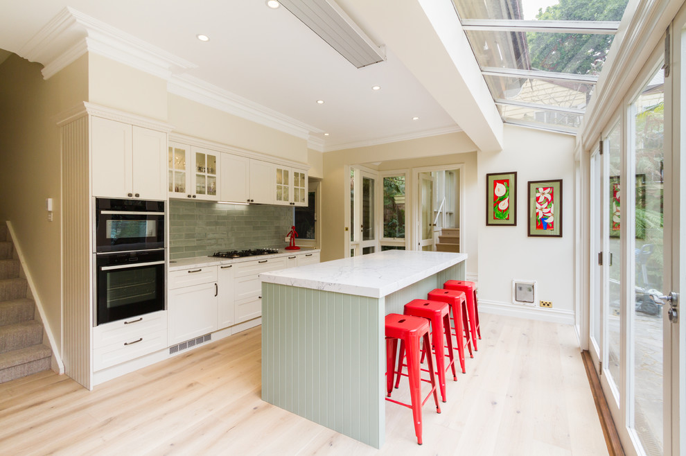 Example of a mid-sized classic galley light wood floor and beige floor eat-in kitchen design in Melbourne with an undermount sink, shaker cabinets, white cabinets, quartz countertops, green backsplash, subway tile backsplash, black appliances, an island and white countertops