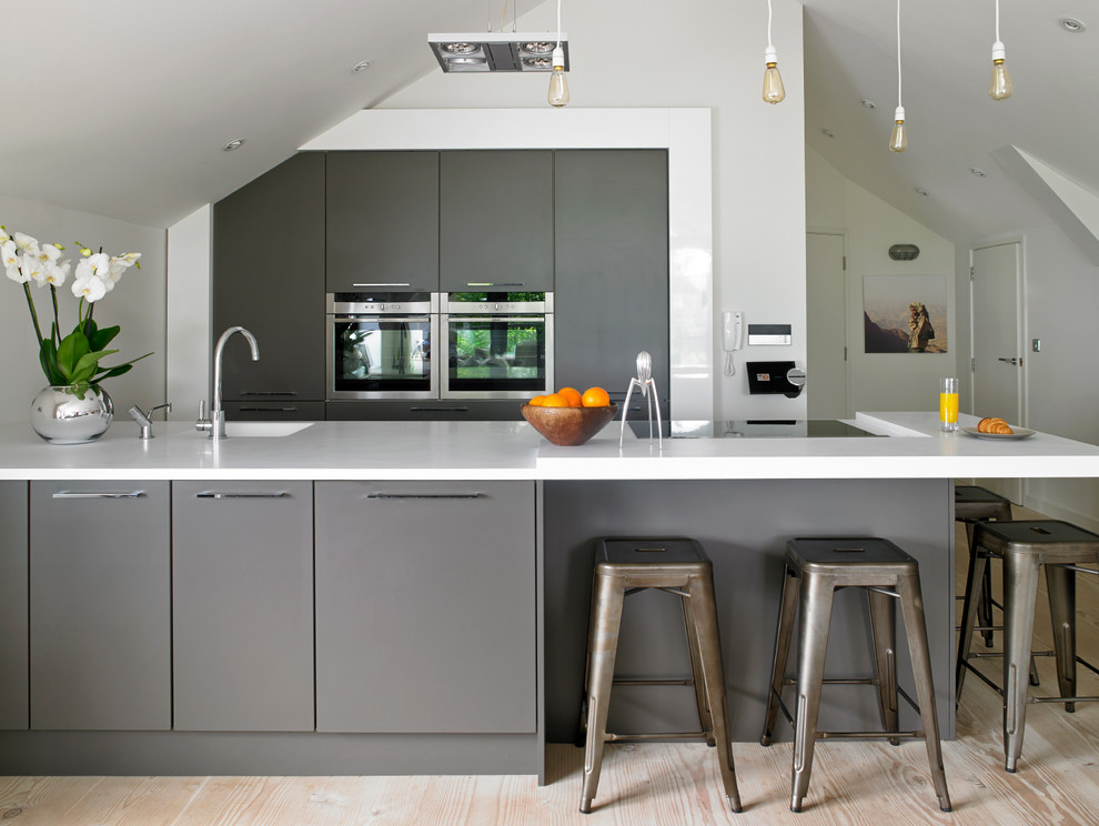 Moderne Küche mit flächenbündigen Schrankfronten, Edelstahlfronten, Küchengeräten aus Edelstahl und hellem Holzboden in Cardiff