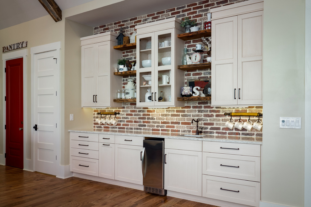 Inspiration for a mid-sized cottage galley medium tone wood floor and brown floor eat-in kitchen remodel in Atlanta with a farmhouse sink, recessed-panel cabinets, beige cabinets, red backsplash, brick backsplash, stainless steel appliances, an island and quartzite countertops