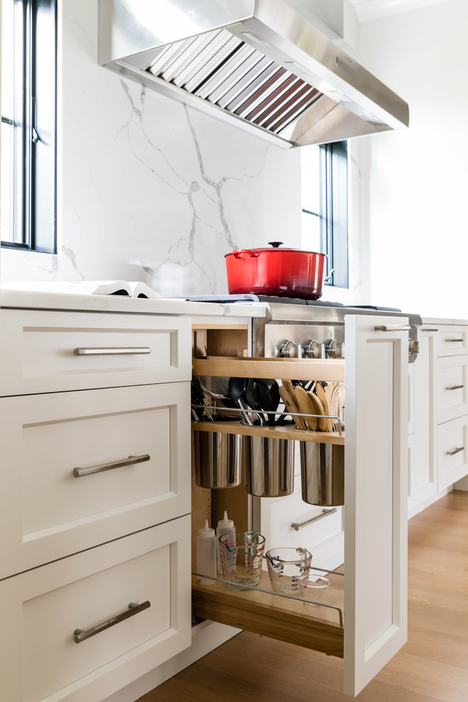 Large country kitchen pantry in Boston with a submerged sink, shaker cabinets, white cabinets, engineered stone countertops, white splashback, stone slab splashback, stainless steel appliances, light hardwood flooring, multiple islands and white worktops.
