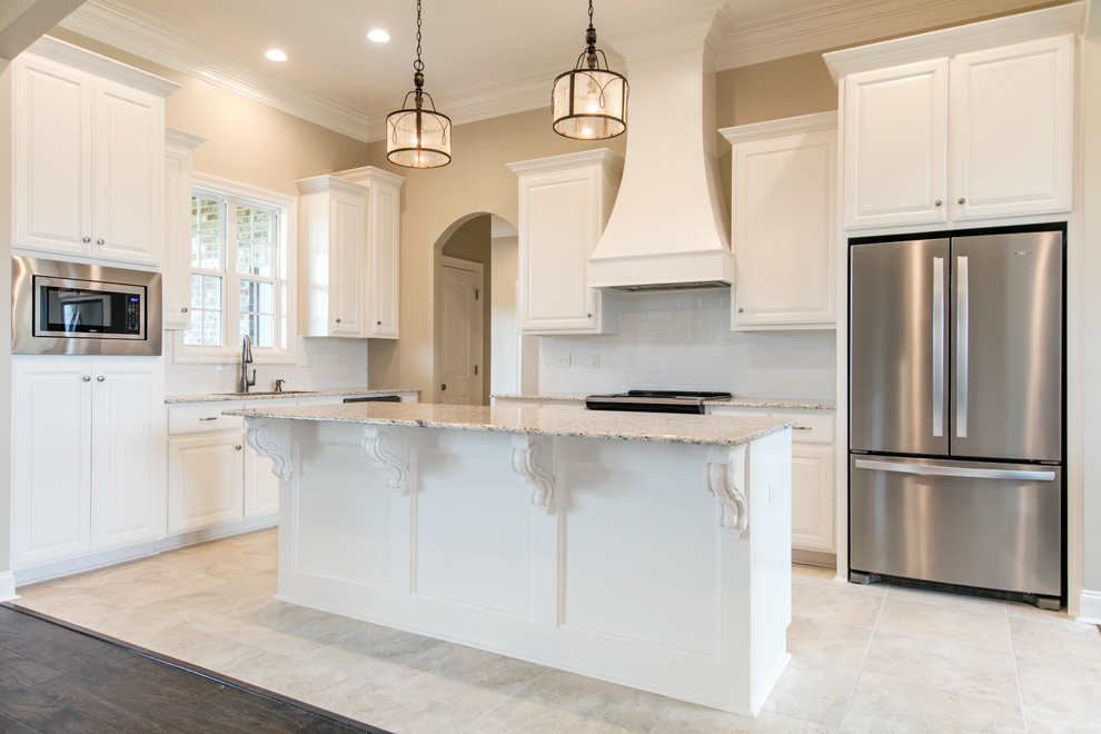 Exempel på ett mellanstort klassiskt vit vitt kök, med en dubbel diskho, luckor med upphöjd panel, vita skåp, granitbänkskiva, vitt stänkskydd, stänkskydd i tunnelbanekakel, rostfria vitvaror, klinkergolv i keramik, en köksö och beiget golv