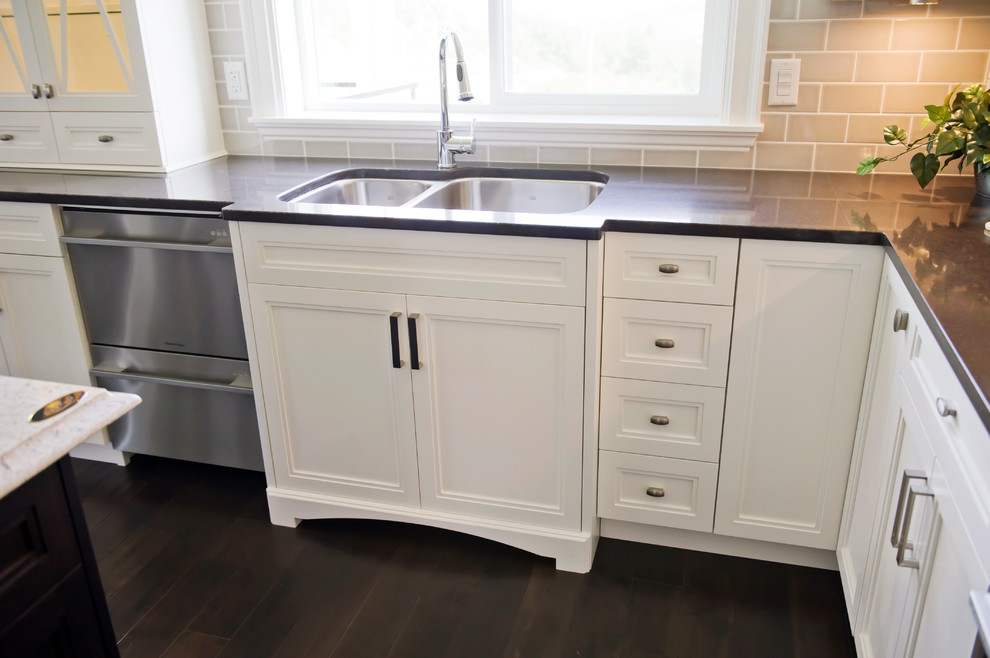 This is an example of a large traditional u-shaped kitchen in Vancouver with a submerged sink, recessed-panel cabinets, white cabinets, granite worktops, grey splashback, metro tiled splashback, stainless steel appliances, dark hardwood flooring, an island, brown floors and black worktops.