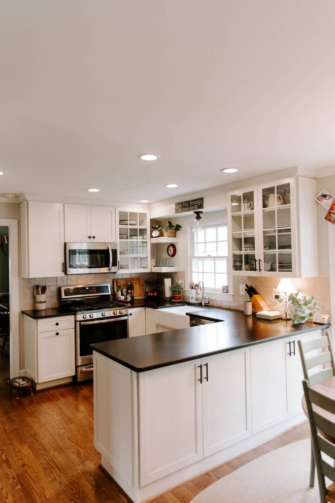 Mid-sized elegant u-shaped eat-in kitchen photo in DC Metro with a farmhouse sink, glass-front cabinets, white cabinets, quartz countertops, gray backsplash, ceramic backsplash, stainless steel appliances and black countertops