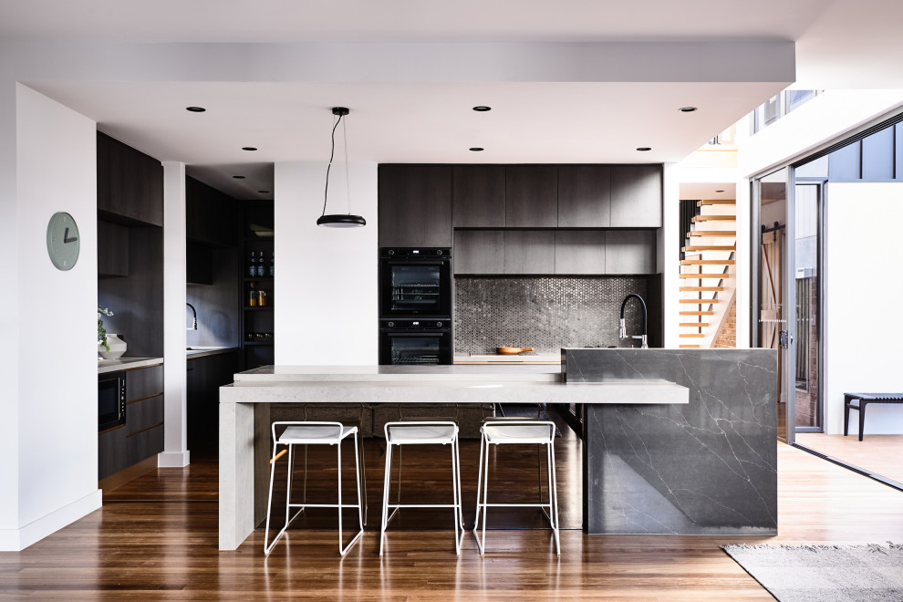 Cette image montre une cuisine ouverte design en U avec un placard à porte plane, une crédence noire, une crédence en mosaïque, un électroménager noir, un sol en bois brun, îlot, un sol marron et un plan de travail blanc.