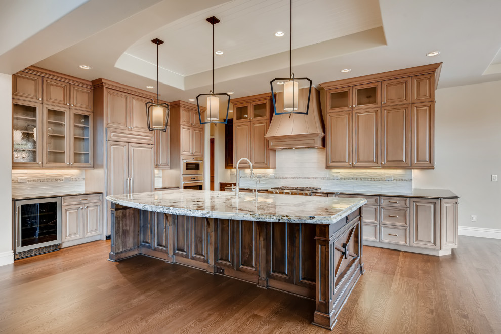 Example of a huge classic l-shaped medium tone wood floor and brown floor open concept kitchen design in Denver with raised-panel cabinets, brown cabinets, granite countertops, beige backsplash, paneled appliances, an island and brown countertops