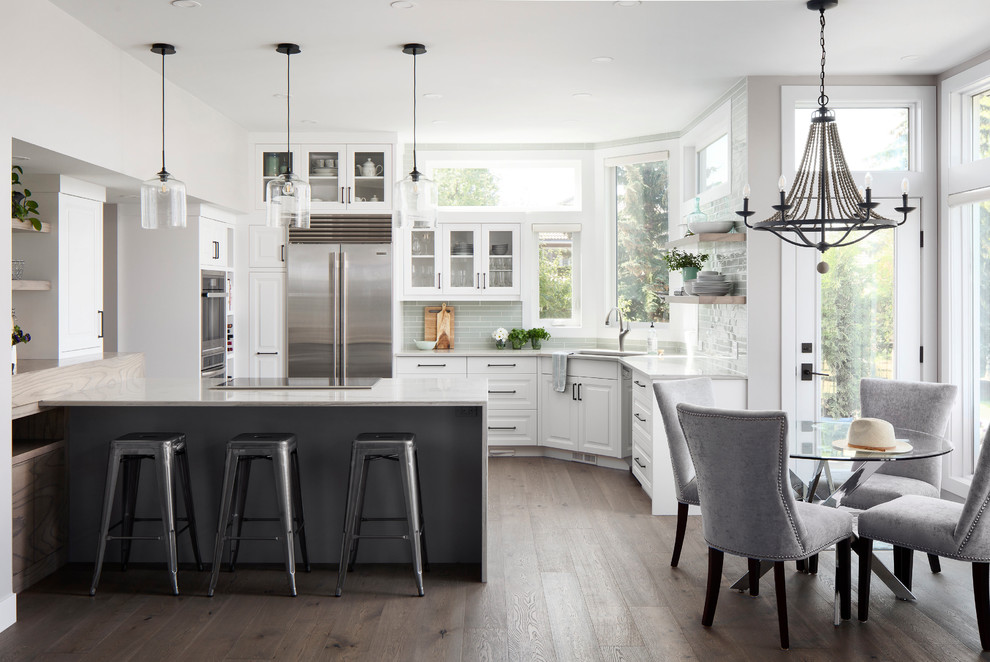 Photo of a medium sized classic l-shaped kitchen/diner in Calgary with a submerged sink, raised-panel cabinets, white cabinets, grey splashback, glass tiled splashback, stainless steel appliances, dark hardwood flooring, a breakfast bar, brown floors and grey worktops.