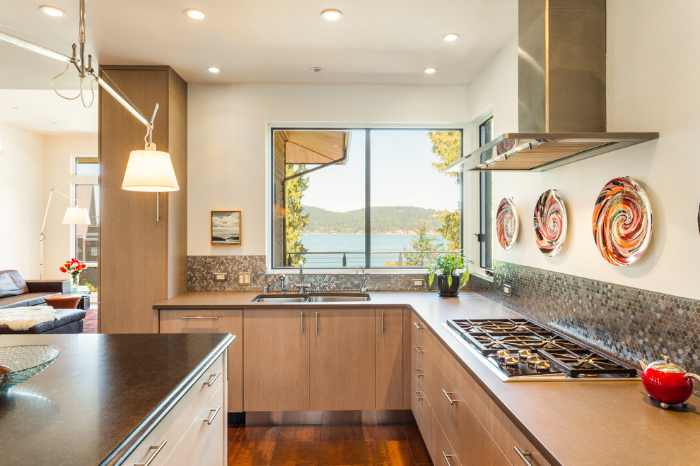 This is an example of a contemporary l-shaped kitchen in Seattle with a double-bowl sink, flat-panel cabinets, light wood cabinets, metallic splashback, stainless steel appliances, medium hardwood flooring and an island.