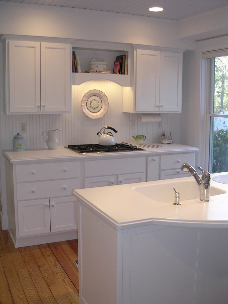 Enclosed kitchen - mid-sized coastal single-wall medium tone wood floor enclosed kitchen idea in Boston with an integrated sink, recessed-panel cabinets, white cabinets, solid surface countertops, white backsplash, white appliances and an island