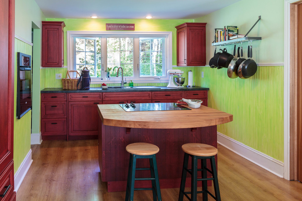 Inspiration for a mid-sized farmhouse l-shaped medium tone wood floor and beige floor open concept kitchen remodel in Miami with a double-bowl sink, raised-panel cabinets, red cabinets, laminate countertops, green backsplash, shiplap backsplash, black appliances, an island and black countertops