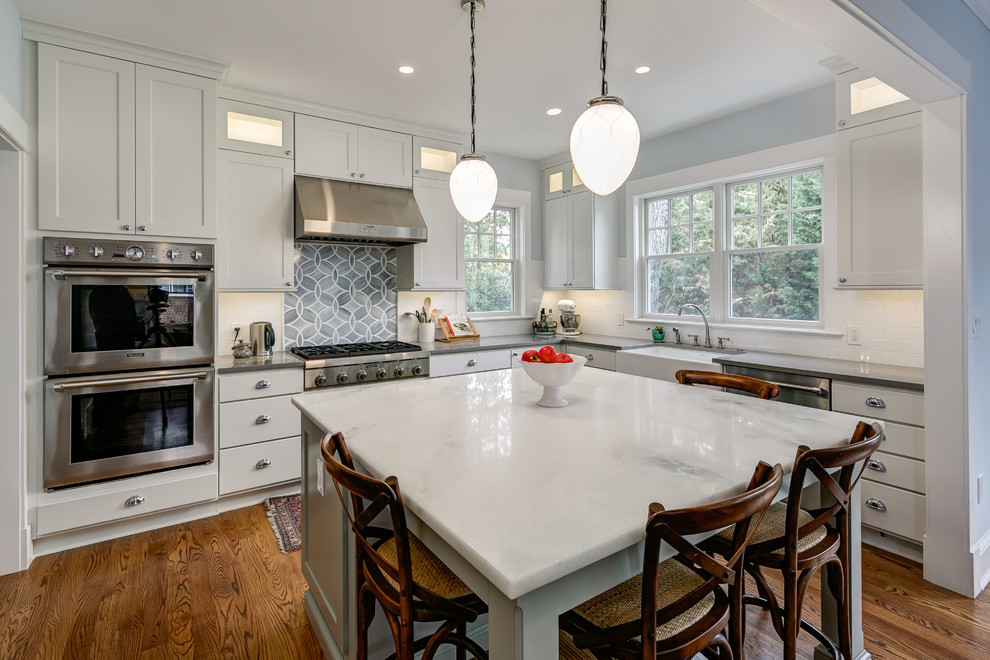 Foto på ett mellanstort amerikanskt kök, med en rustik diskho, skåp i shakerstil, vita skåp, marmorbänkskiva, vitt stänkskydd, stänkskydd i tunnelbanekakel, rostfria vitvaror, mellanmörkt trägolv och en köksö