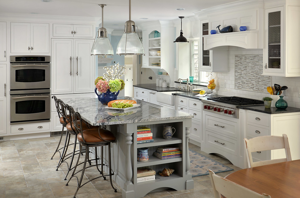 Example of a beach style l-shaped eat-in kitchen design in Boston with a farmhouse sink, shaker cabinets, white cabinets, white backsplash, subway tile backsplash, paneled appliances and an island